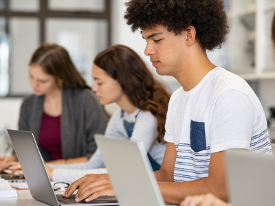 Student werkt aan een laptop. Naast hem zitten 2 andere studenten met een laptop.