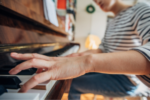 Iemand zit achter de piano en drukt met de vingers op een toets