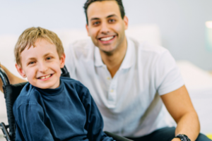 kind in rolstoel met daarachter begeleider