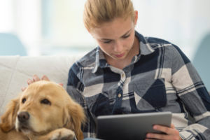 jong persoon leest op ipad met hond naast zich