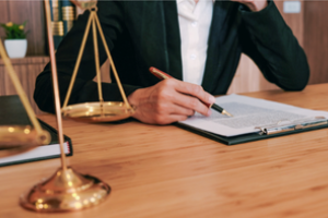 persoon aan bureau met pen in de hand en tekst op papier en een weegschaal