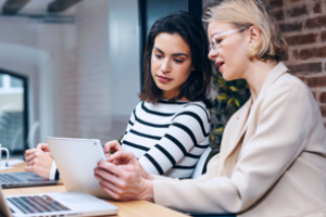 twee mensen overleggen terwijl ze samen kijken op een ipad, gezeten aan bureau met laptop
